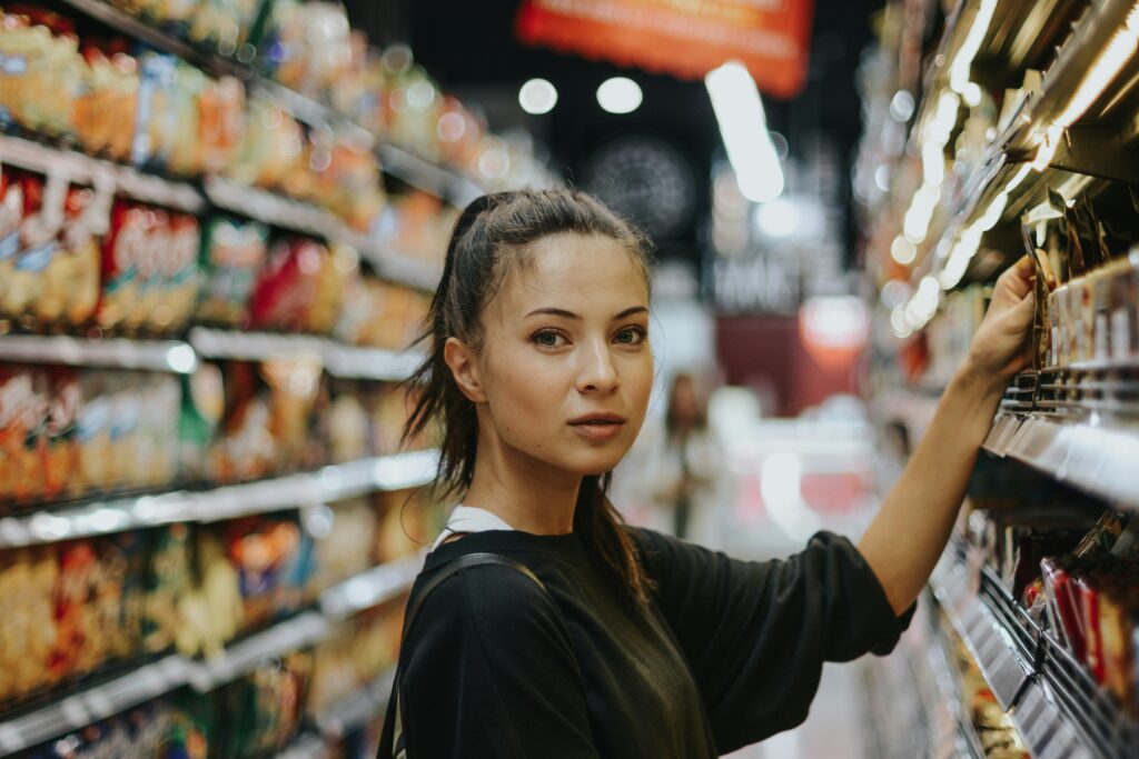 Woman in supermarket picking a product from the shelf and looking straight to camera